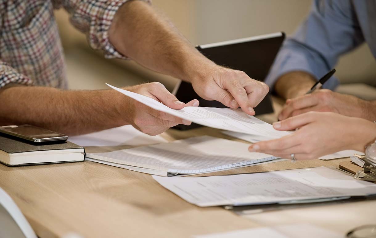 Three sets of hands reviewing and picking up documents ready to sign.
