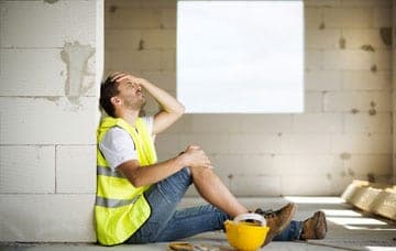 Construction worker sitting on the floor and holding his head and leg