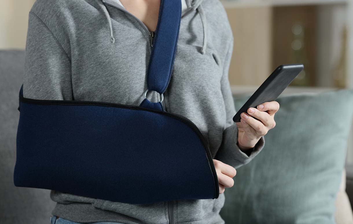 Woman with injured arm in a sling holding a mobile phone.